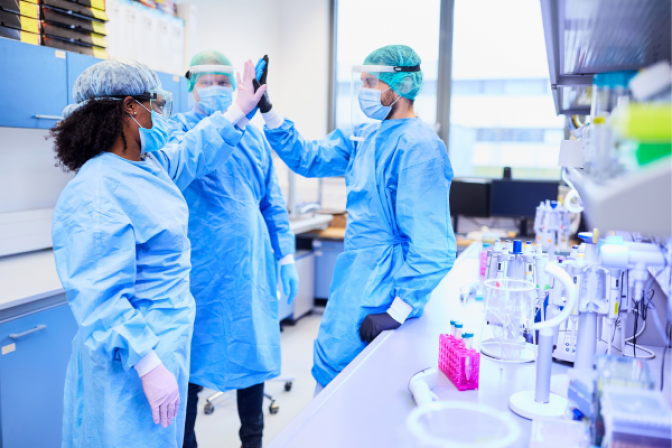 Three scientists in protective gear high fiving