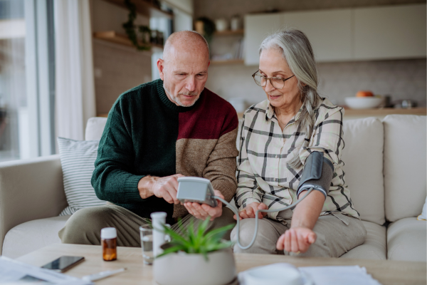 An older person helping their partner use an out-home blood pressure monitor.