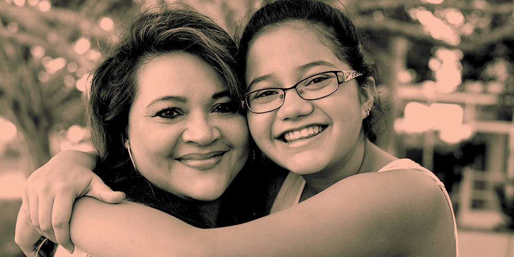 Mom and daughter hugging, smiling, and looking camera