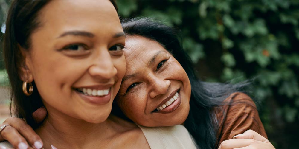 Mom and daughter hugging, smiling, and looking camera