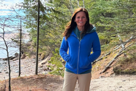 Sarah standing in a forest by a lake