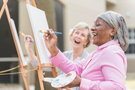 Two older people laughing while painting