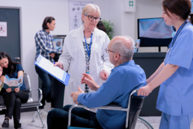 Person in wheelchair speaking with doctor holding paperwork