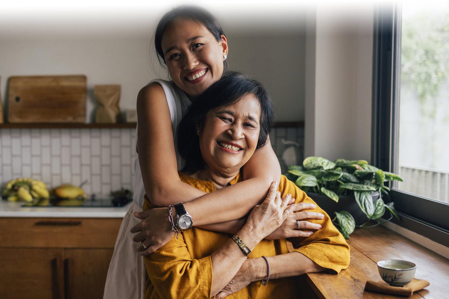 Woman hugging her mother in the kitchen and smiling