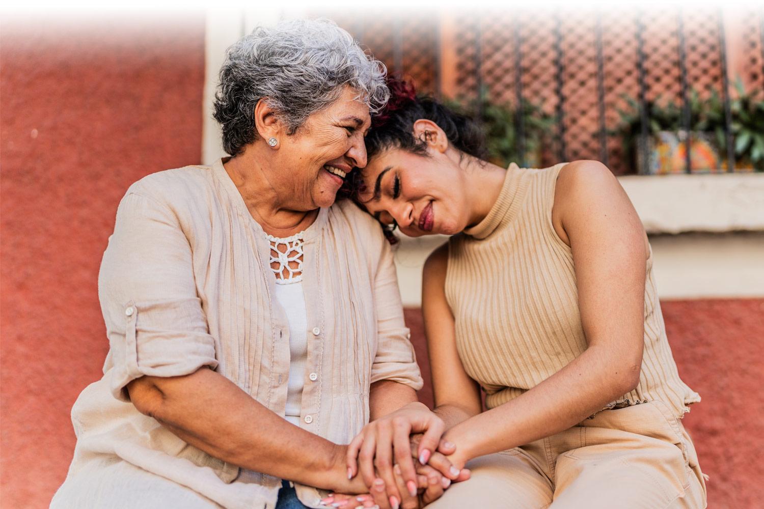 Hispanic grandmother sitting with granddaughter, with her head resting on her grandmother's shoulder 