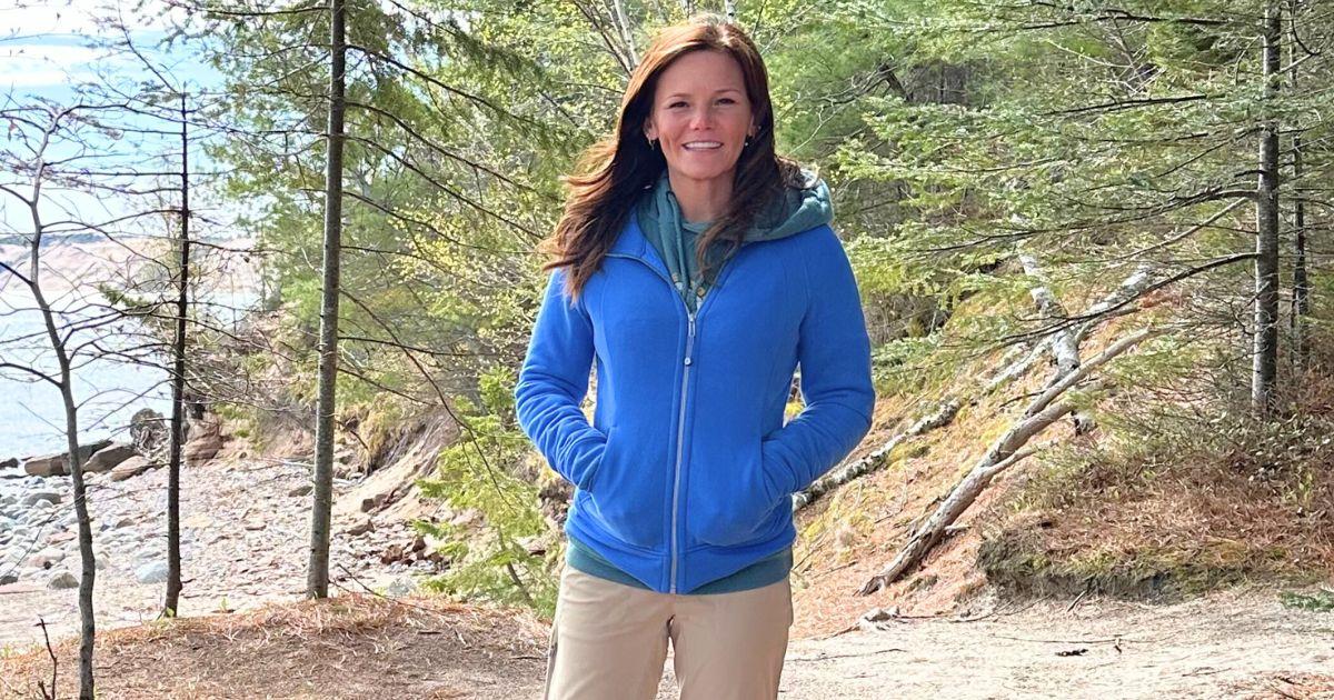 Sarah Kaspari standing in the forest with lake behind her.