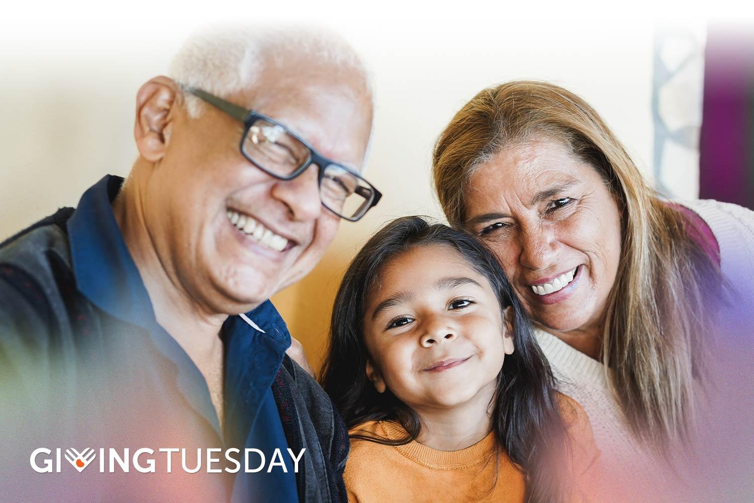 Hispanic grandparents and granddaughter smiling together for the camera, with Giving Tuesday logo