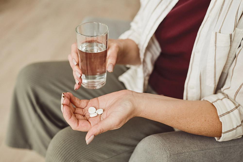 Un adulto con pastillas y agua en las manos