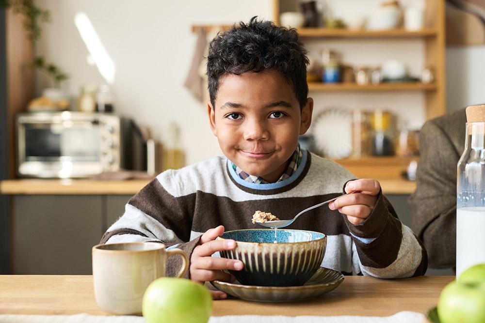 Un niño feliz desayunando cereales en la mesa de la cocina
