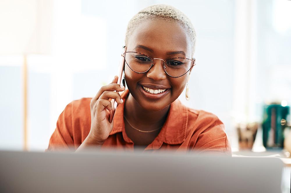 Woman speaking on the phone looking at a computer, feeling connected