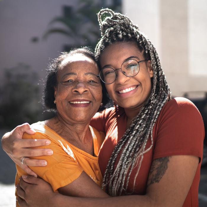 Daughter hugging mom while both are smiling at camera